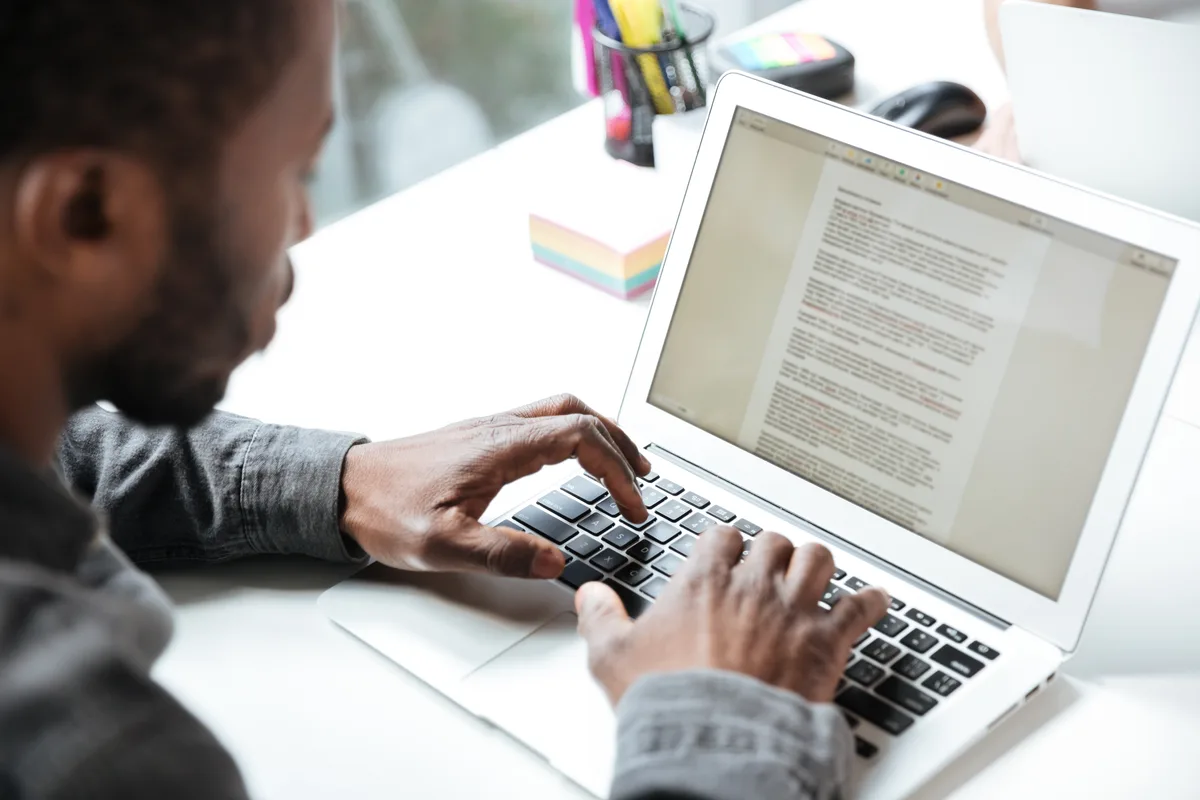Homme attablé devant un ordinateur portable, en train de rédiger un article dans un traitement de texte