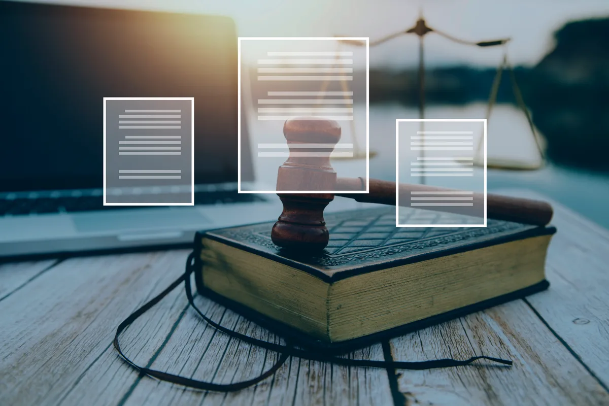 Marteau de juge posé sur un livre de droit, à côté d'un ordinateur portable et d'une balance de la justice, avec des icônes de documents en surimpression